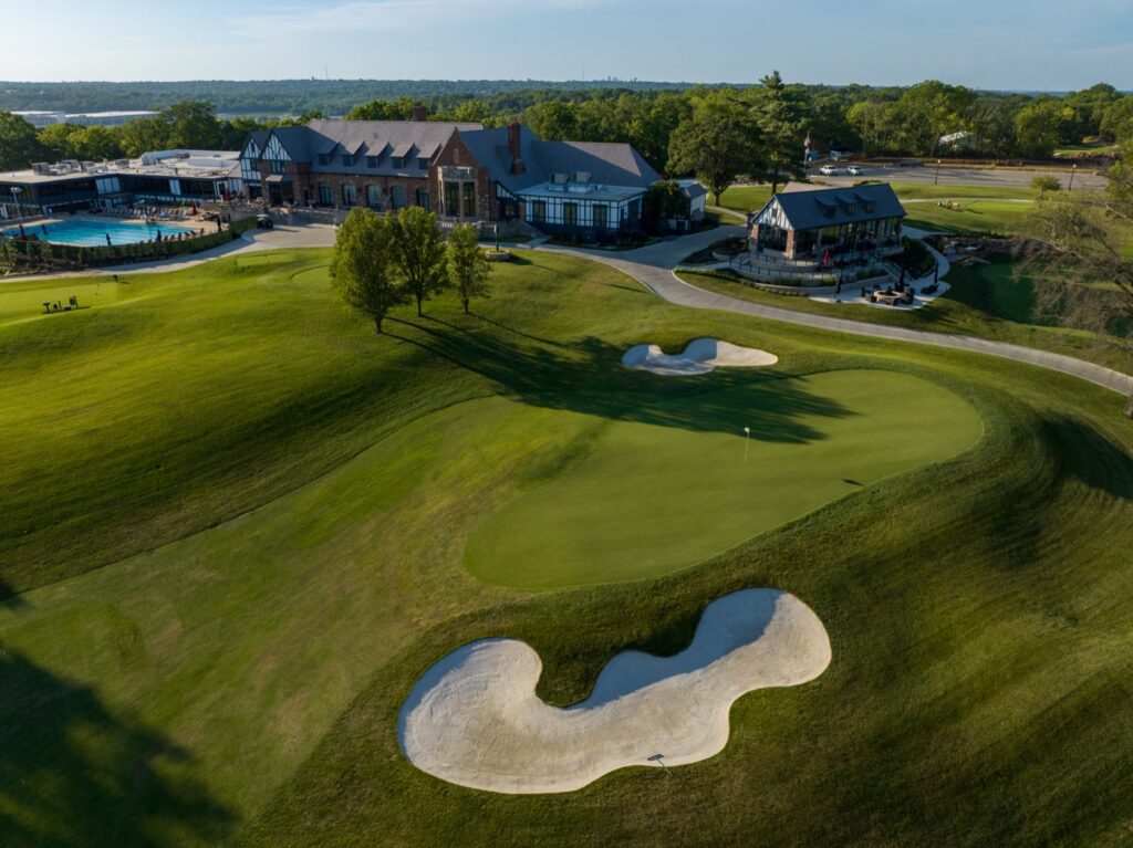 Aerial view of a historic Tudor Revival clubhouse and golf course